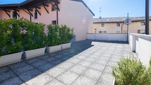 A rooftop terrace with potted plants, a clear sky, and buildings in the background. - Appartamento Lilli (Manerba del Garda)