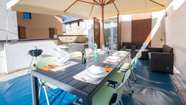 An outdoor dining area with a table set for four, surrounded by chairs, under a large umbrella. - Appartamento Lilli (Manerba del Garda)