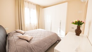 A bedroom with a bed, a nightstand, a desk, a vase with flowers, and a wardrobe. - Appartamento Lilli (Manerba del Garda)