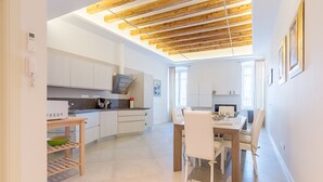 Una cocina moderna con armarios blancos, techo de madera y un comedor con mesa y sillas.