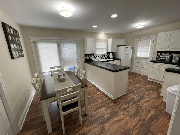 A modern kitchen with a dining area, white cabinetry, a central island, and a black countertop.