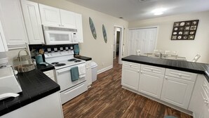 A kitchen with white cabinets, a black countertop, a stove, and a microwave.