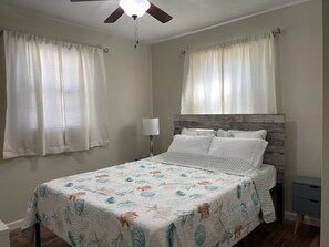 Ein Schlafzimmer mit Bett, Vorhängen, Deckenventilator und Nachttisch.
