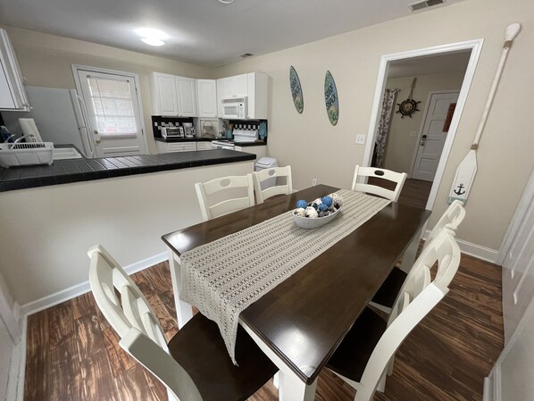 A dining area with a dark wooden table, white chairs, and a crocheted table runner. - Home Sweet Home, 7 Minutes From Carolina Beach (Wilmington)