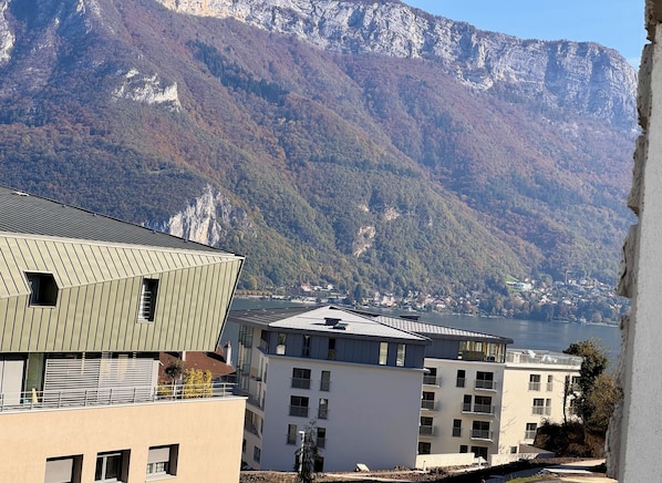 A modern building with a sloped roof and a balcony, overlooking a lake and mountains.