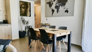 A modern dining area with a wooden table and black chairs, a world map on the wall, and a Buddha statue. - Le petit marquisat à deux pas du lac (Annecy)