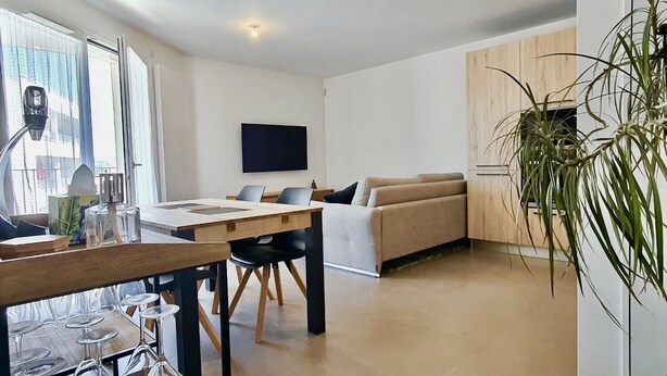 A modern living room with a wooden dining table, a sofa, and a TV mounted on the wall. - Le petit marquisat à deux pas du lac (Annecy)