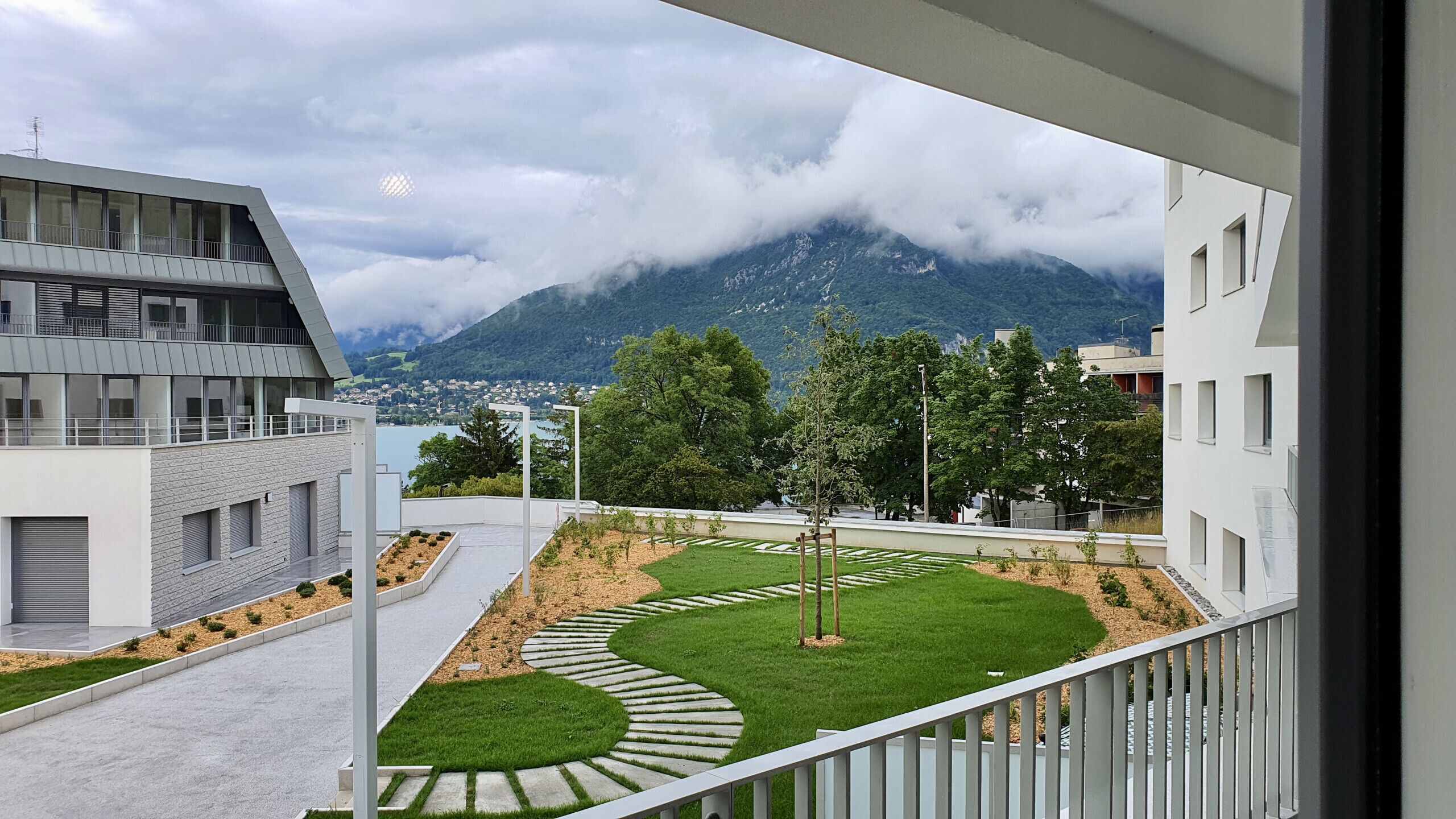 A modern building with a balcony overlooking a landscaped garden and a mountainous landscape.