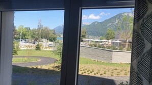 A view through a window of a parking area with a curved road, a stone wall, and a mountainous landscape in the background.