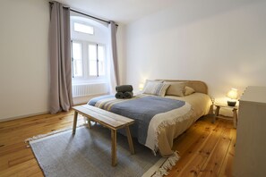 Un dormitori amb llit, una panxa, una taula de nit, una làmpada i una finestra amb cortines.