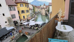A riverside café with outdoor seating, a wooden fence, and a mountain backdrop. - Le Thiou / Old Town - Nearby Lake (Annecy)
