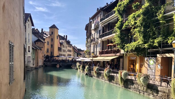 A canal with buildings on either side, a bridge, and a restaurant with outdoor seating. - The Lodge 106 apartment at the foot of Semnoz (Sévrier)