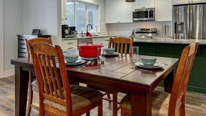 Cozinha moderna com armários brancos, eletrodomésticos de aço inoxidável e mesa de jantar de madeira com cadeiras.