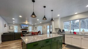 Uma cozinha moderna com armários verdes, bancada de mármore e iluminação pendente.