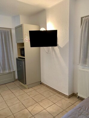 Une petite pièce équipée d’un téléviseur fixé au mur, d’un mini-réfrigérateur, d’un four à micro-ondes et d’un radiateur.
