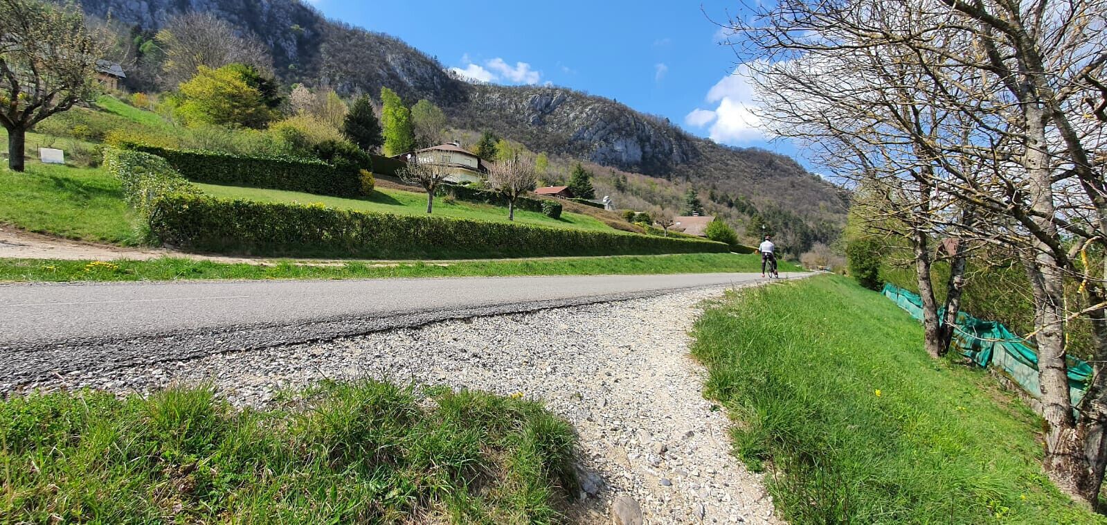 A rural road with a cyclist, green hedges, and a mountain backdrop.