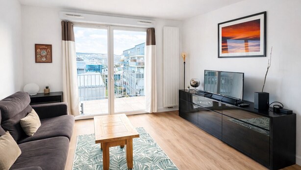 Ein modernes Wohnzimmer mit einer Couch, einem Couchtisch, einer TV-Konsole und einem großen Fenster mit Blick auf die Stadt.