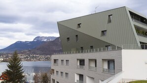 Un edificio moderno con un design angolare unico, un balcone e vista su un lago e montagne sullo sfondo.