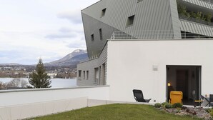 Un edificio moderno con tetto spiovente, un balcone con ringhiera e vista su un lago e montagne sullo sfondo.