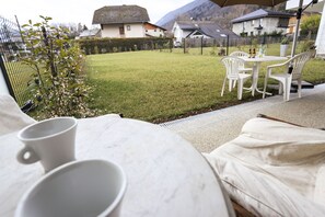 A cozy outdoor seating area with a table and chairs, a grassy lawn, and a view of houses in the background. - The Boubioz Garden (Sévrier)
