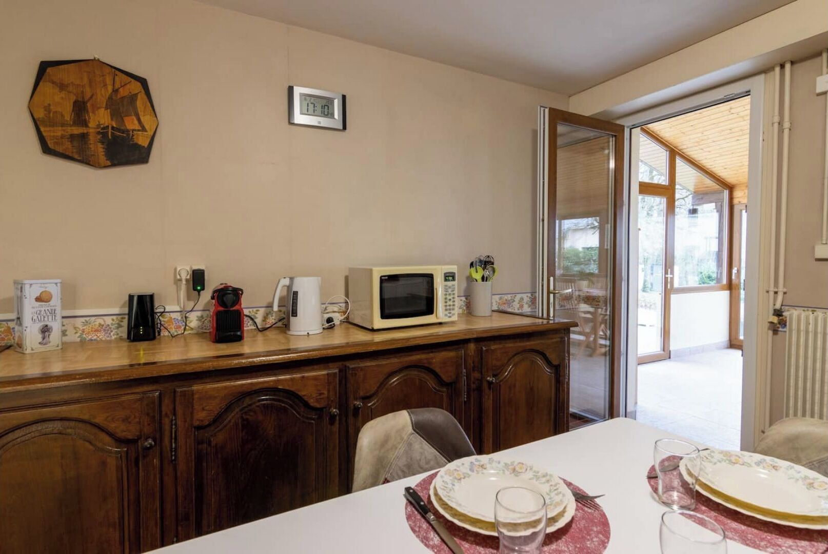 Un coin repas avec une table en bois, un four à micro-ondes, une machine à café et une horloge au mur.