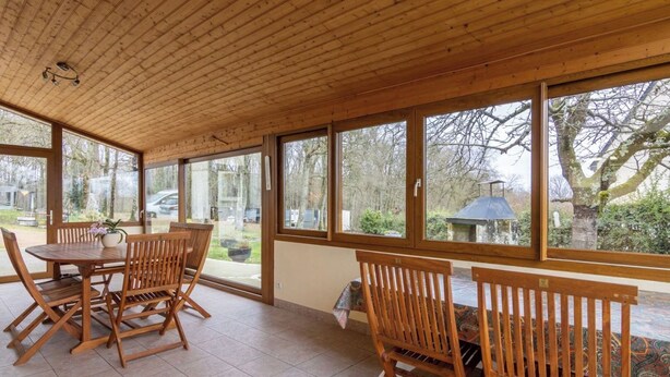 Une terrasse couverte avec un plancher en bois et de grandes fenêtres.