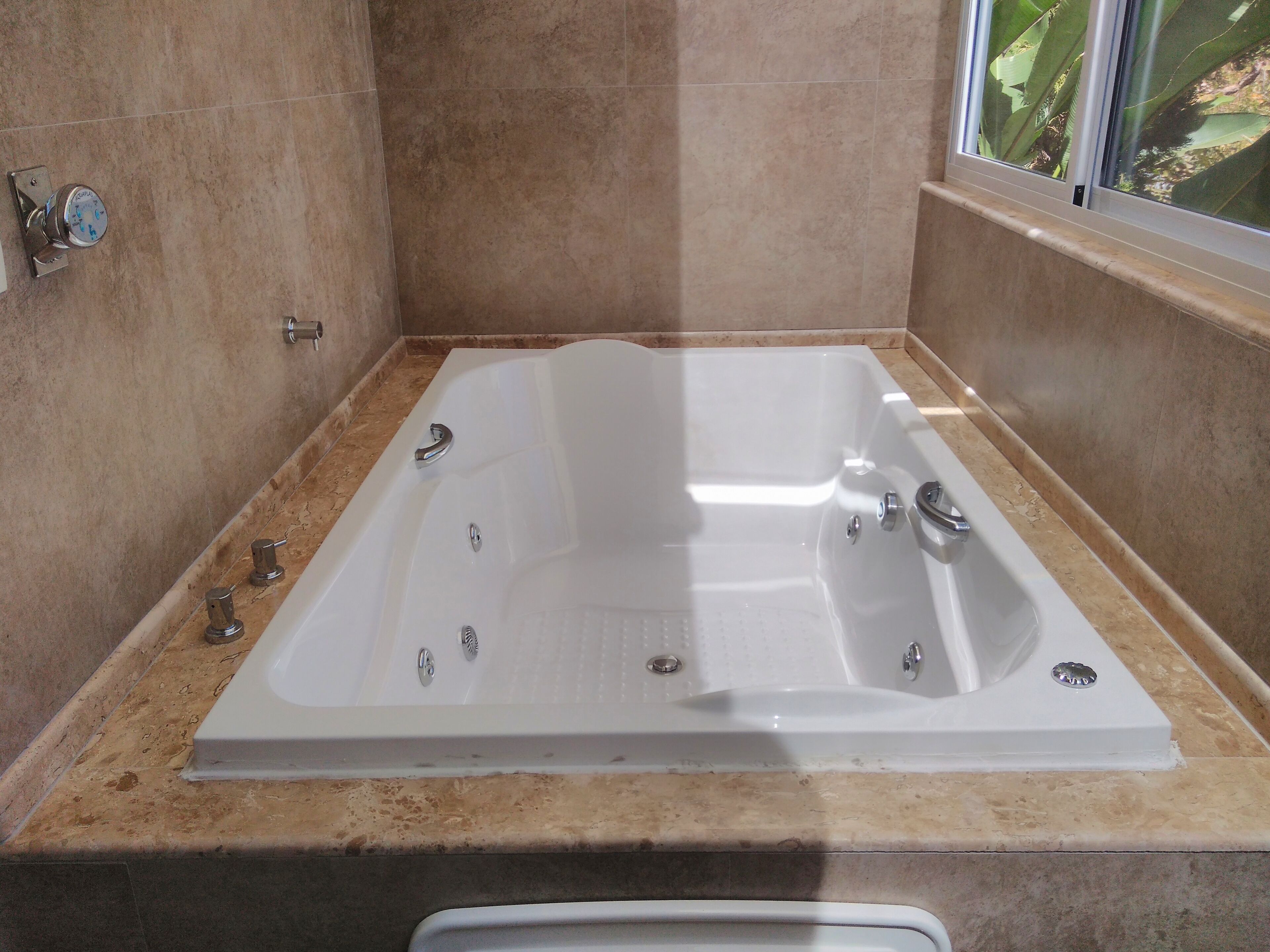 Un baño con una bañera grande, encimera de mármol y ventana con vistas a la vegetación.