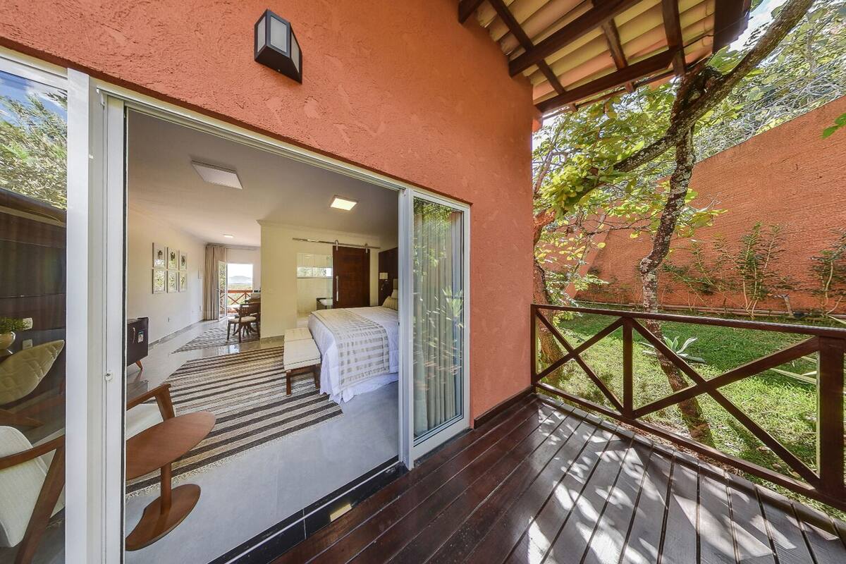 Une chambre à coucher ouverte, comprenant un lit, un bureau et une chaise, qui donne sur un balcon offrant une vue sur un jardin.