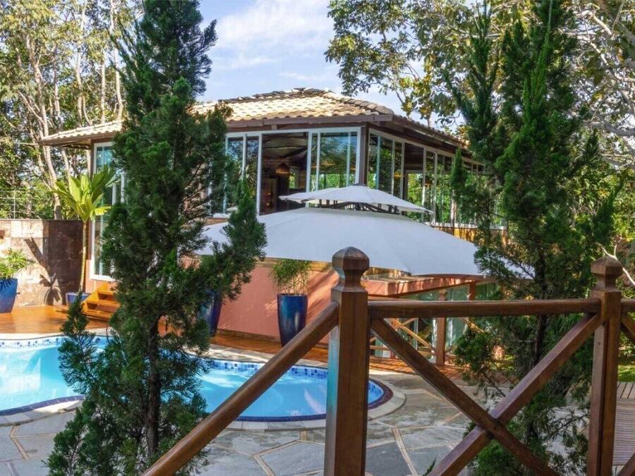Zona de piscina con área de descanso cubierta, piscina y vegetación circundante.