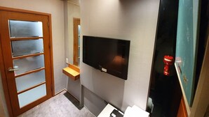 A bathroom with a wooden door, a mounted TV, and a mirror. - Dalgona Guesthouse (Seoul)