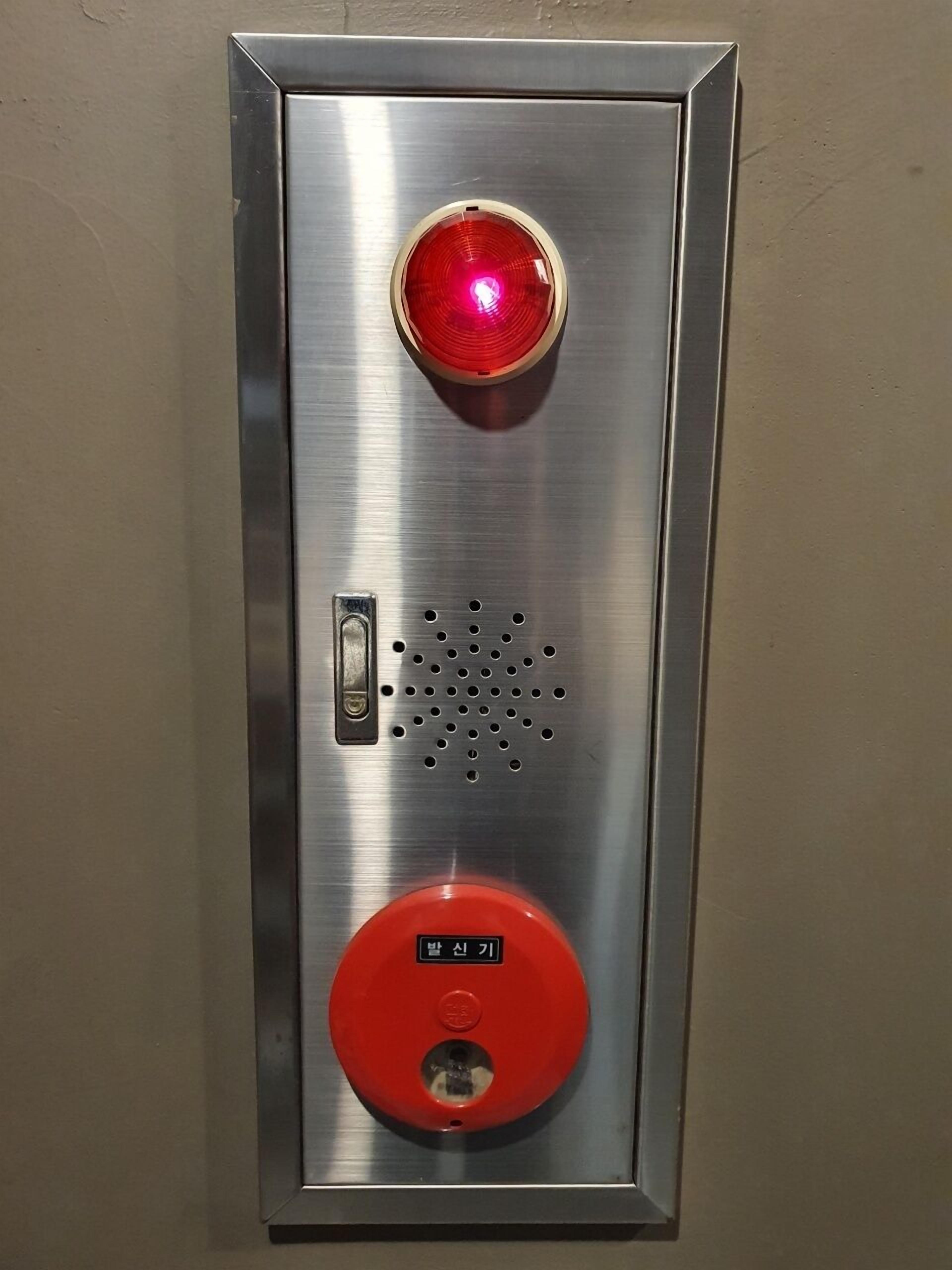 Un panel de control de ascensor metálico con un botón de emergencia rojo y un teclado numérico.