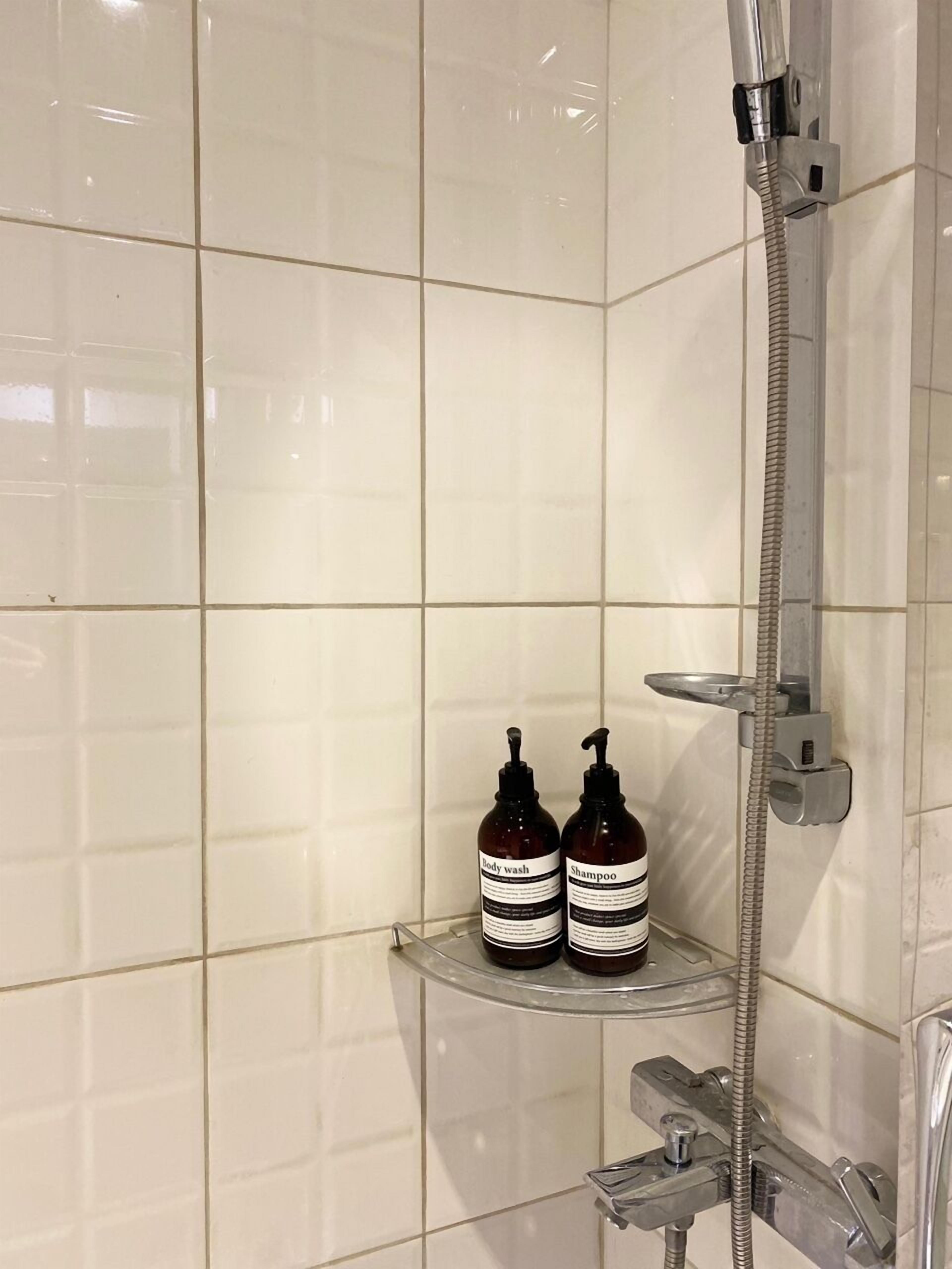 Douchegedeelte met een chroomdouchekop en -slang, en twee flessen douchegel en shampoo op een plank.