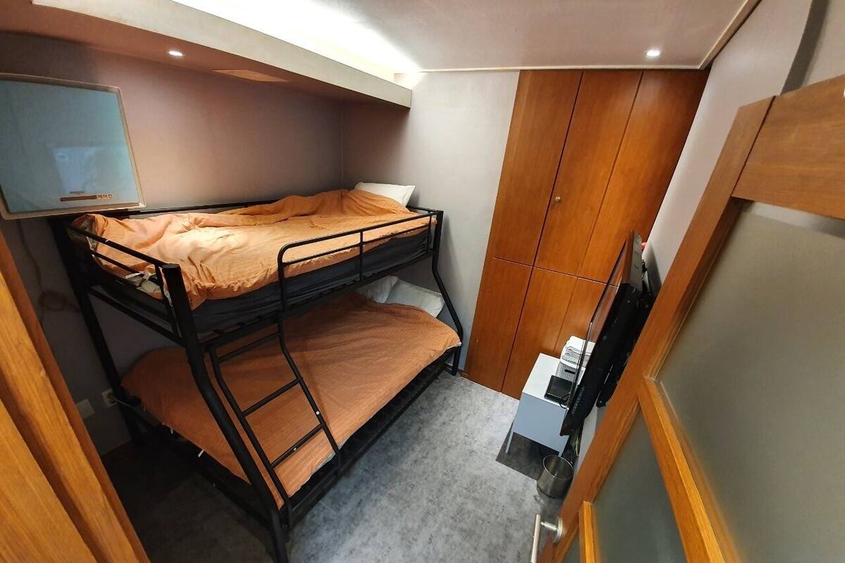 Una habitación compacta con literas, un kitchenette pequeño y un televisor montado en la pared.