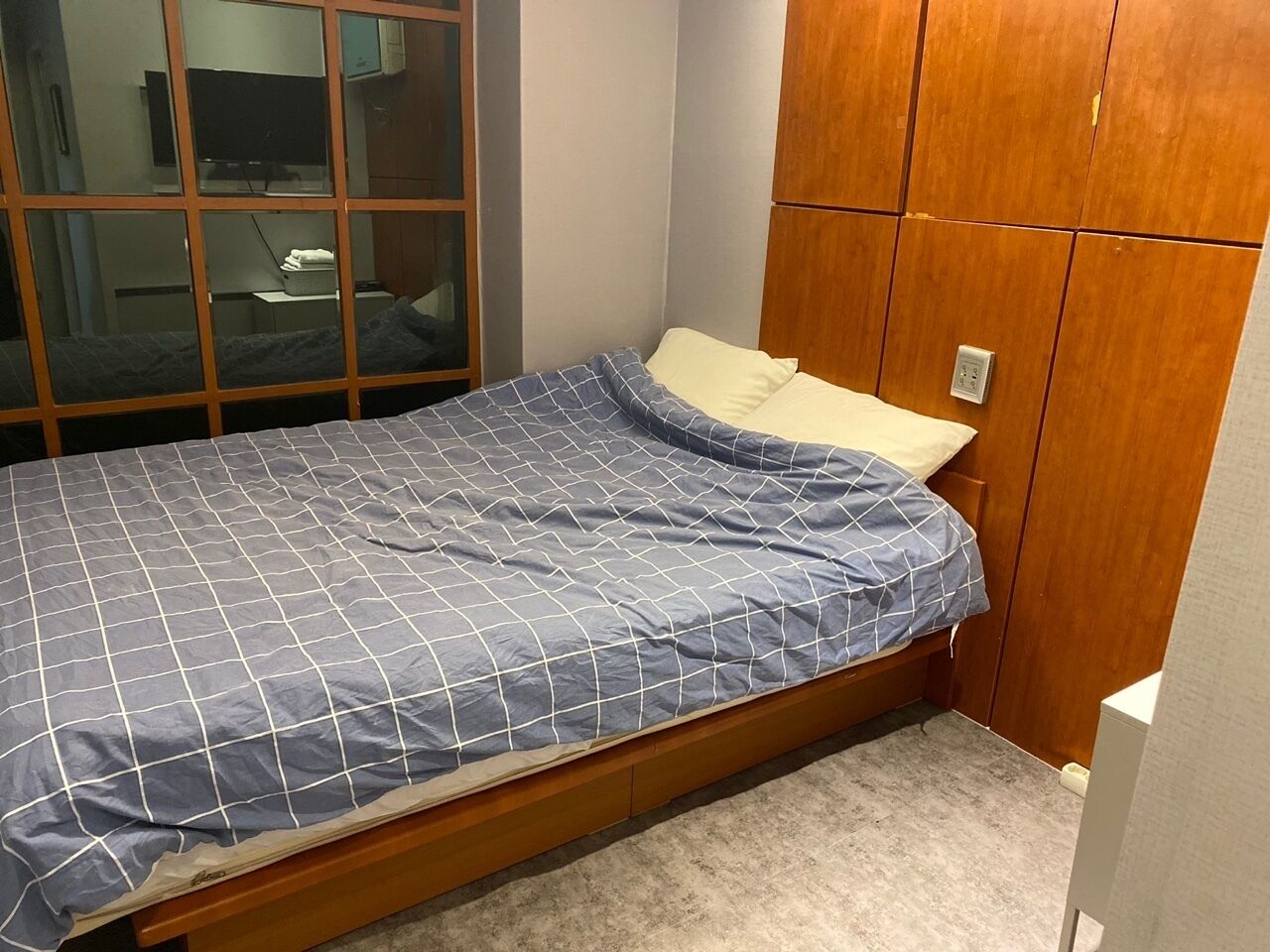 A single bed with a blue and white checkered bedspread, a wooden headboard, and a wooden wardrobe with a mirror.