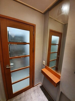 A room with a wooden door with frosted glass panels, a mirror, and a small wooden shelf. - Dalgona Guesthouse (Seoul)