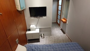 A compact hotel room with a bed, a TV mounted on the wall, a small desk with a lamp, and a shoe rack. - Dalgona Guesthouse (Seoul)
