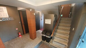 A hallway with a staircase, a fire extinguisher, and a trash bin. - Dalgona Guesthouse (Seoul)