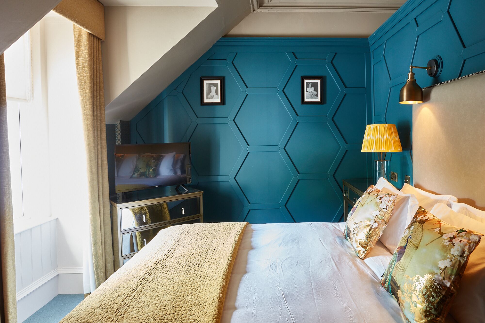 Ein modernes Schlafzimmer mit einer Türkis-farbenen Akzentwand, einem Bett mit gemusterten Kissen, einer Kommode und einem Fernseher.