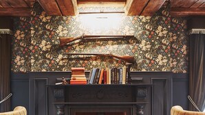 Een gezellige kamer met een open haard, houten balken en een bloemenbehang.