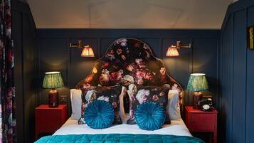 A bedroom with a teal bedspread, floral headboard, and two bedside lamps.