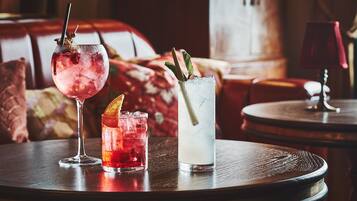 Three drinks on a round table in a room with a sofa and a lamp in the background.