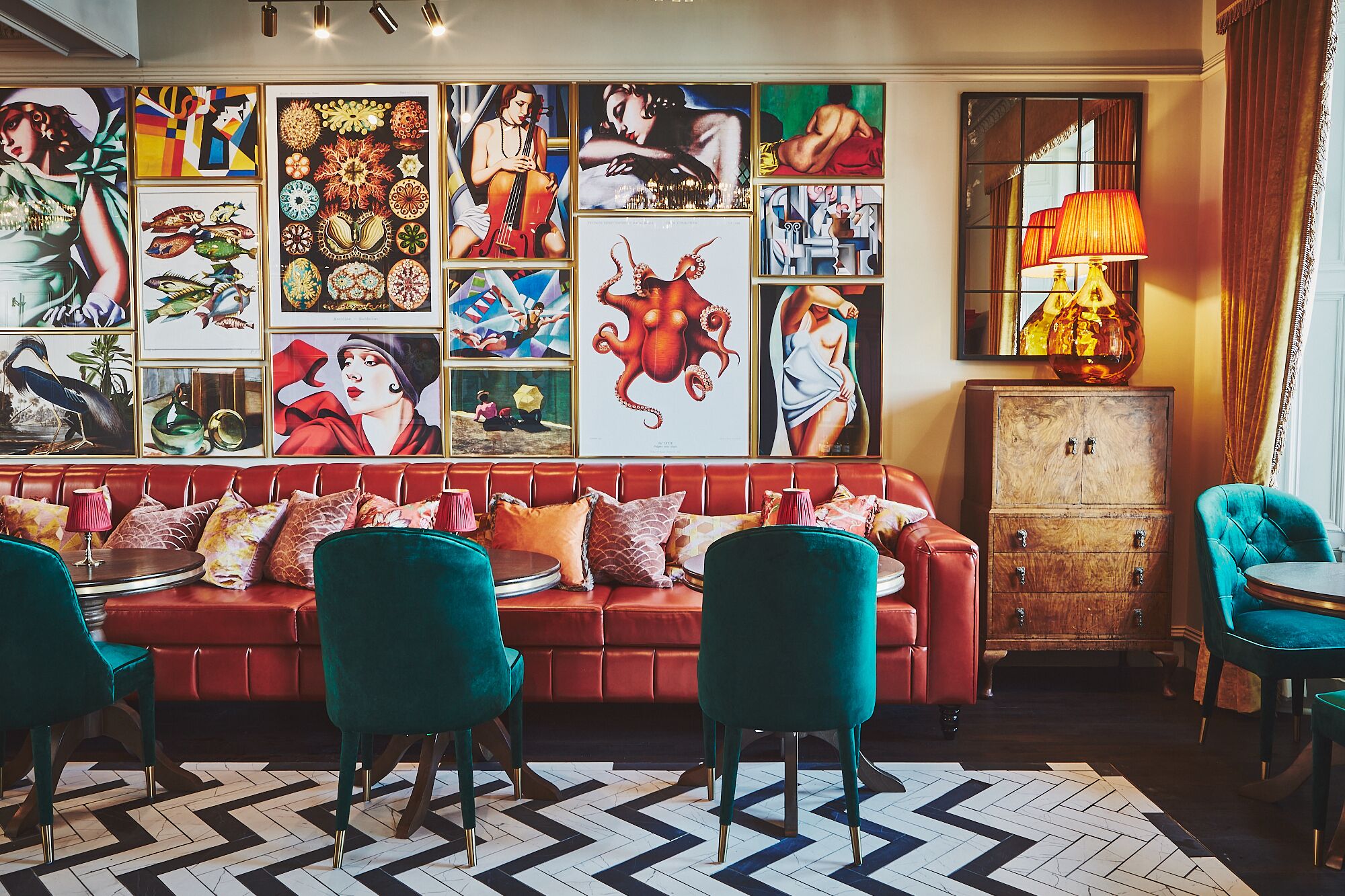 Un espacio lounge acogedor con un sofá rojo, sillas color turquesa y un suelo estampado.
