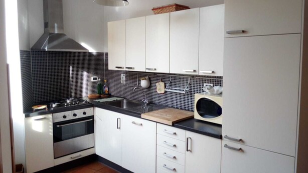 A modern kitchen with white cabinets, a black tiled backsplash, a stainless steel range hood, a microwave, and a sink. - Large Vatican Apartment with 3 bedroom (Rome)