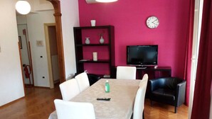 A dining area with a table, chairs, a television, and a shelf with decorative items. - Large Vatican Apartment with 3 bedroom (Rome)