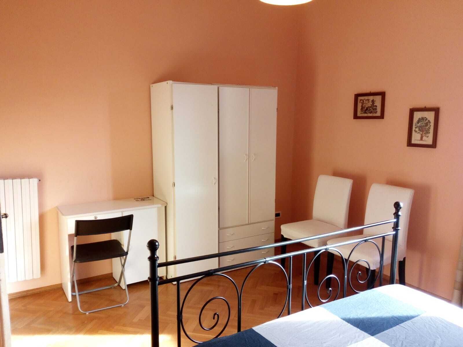 Un dormitorio con cama, escritorio, silla, armario y dos cuadros en la pared.