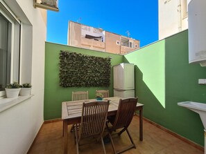 A small patio with a table and chairs, a refrigerator, and a green wall with a leafy decoration. - APARTMENT WITH 2 TERRACES AND PARKING IN THE SAME BUILDING (Cartagena)
