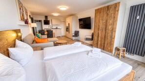 A hotel room with a bed, a sofa, a small table, a chair, a TV, and a kitchen area. - Smart Resorts - Maison Brilliant - Studio 610 with balcony, max. guests (Winterberg)