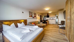 Une chambre d’hôtel avec un grand lit, un canapé, une petite table et, au fond, un coin cuisine.
