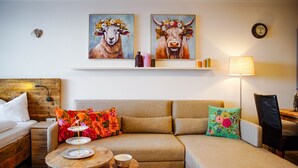 Un salon chaleureux avec un canapé, une petite table ronde et une lampe. Deux tableaux représentant des animaux sont accrochés au mur.
