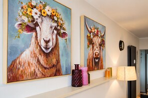 Two paintings of a sheep on a wall, a clock, and a shelf with decorative items. - Smart Resorts - Maison Brilliant - Studio 610 with balcony, max. guests (Winterberg)